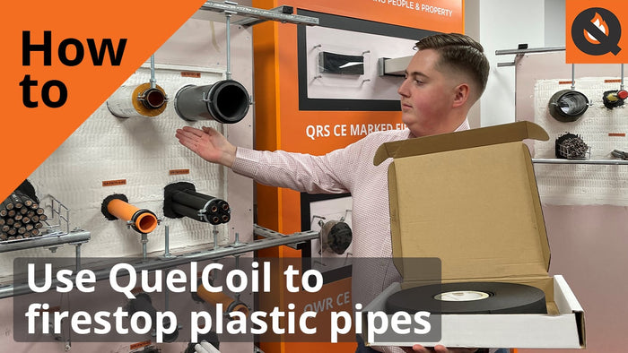 Glenn Hutchins, Technical, pointing to a Quelfire demo board. He is holding the QuelCoil. The image is titled, 'How to use QuelCoil to firestop plastic pipes'.