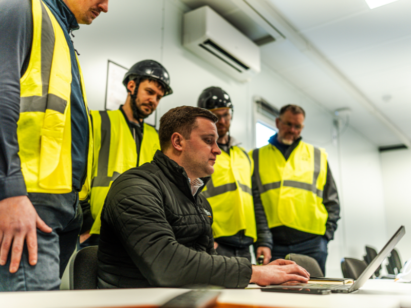 Craig Wells, Sales Director, talking through the QuelSelector Tool with construction professionals wearing yellow high-vis vests.