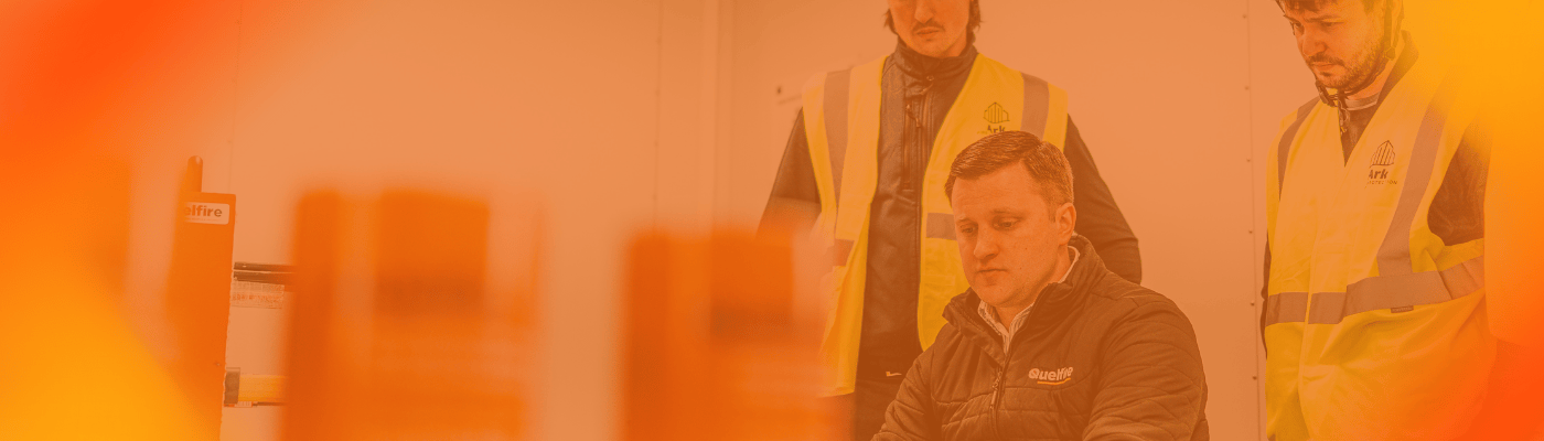 Two people wearing high-visibility vests in a training room setting, watching Sales Director, Craig, deliver a CPD training session.
