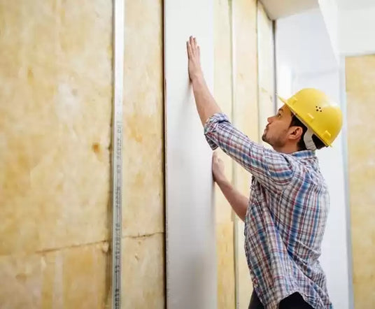 Man in a checked shirt and hard hat is installing a piece of drywall.