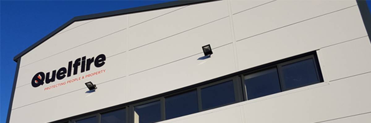 Photo of the old Quelfire premises in Sandbach. A grey building with the Quelfire logo on the front. A row of windows sits below.