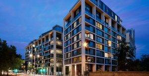 A modern, multi-storey building with multiple illuminated rooms at dusk.