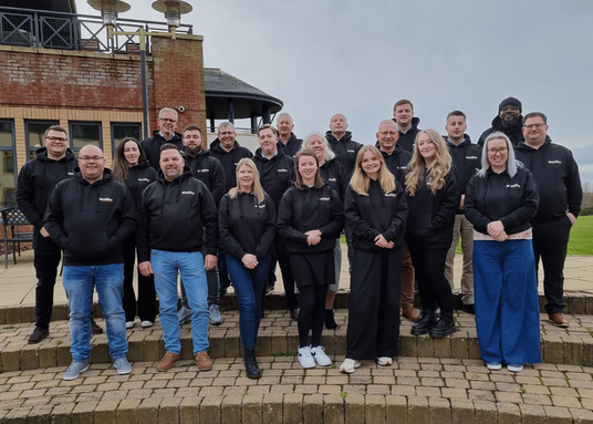 Quelfire's team in branded black hoodies standing outdoors on a brick patio with a building and greenery in the background.