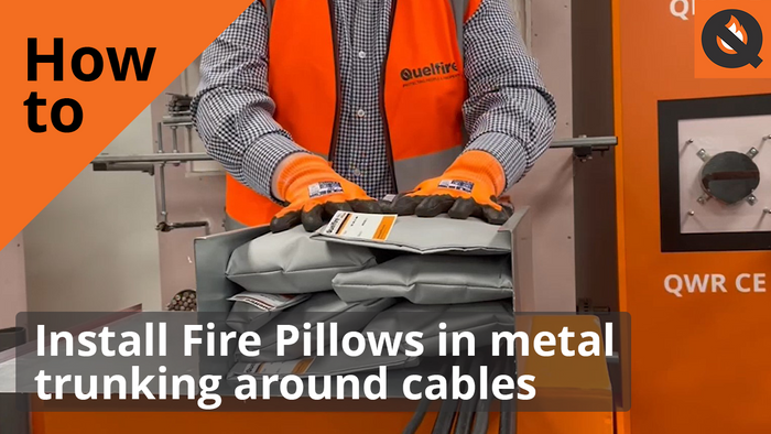 Glenn Hutchins, Technical, showing how to install Quelfire fire pillows. He is wearing an orange hi-vis vest and orange safety gloves. The text says, 'How to install fire pillow in metal trunking around cables'.