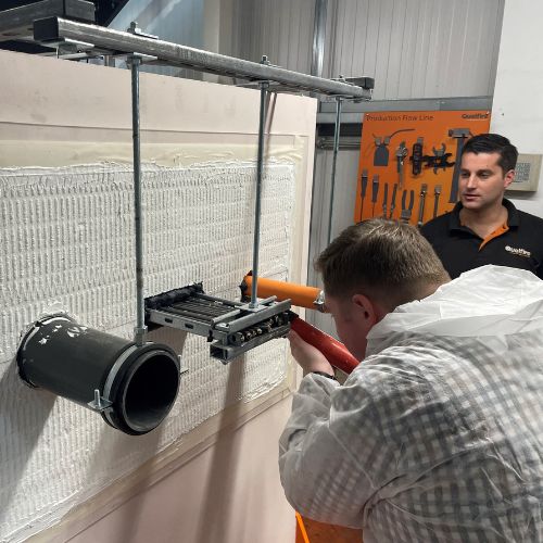 Glenn Hutchins, member of the technical team, wearing white overalls, while practicing an install of firestopping products.