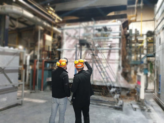 Image of a Quelfire fire test. Keith (Managing Director) and Darryl (Commercial & Development Manger) can be seen wearing orange hard hats, pointing to the test. The background is blurred. 