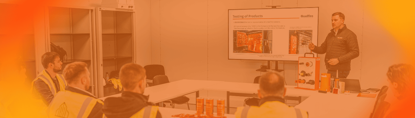 An orange gradient screen featuring Craig Wells, Sales Director, presenting to five customers. He is standing in front of a screen with Quelfire products next to him. 