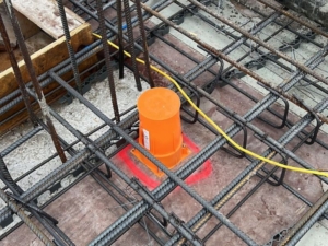 Cast-in fire collar installed within reinforced concrete formwork, surrounded by rebar mesh, with an orange protective cap and red marking to indicate fire protection placement.